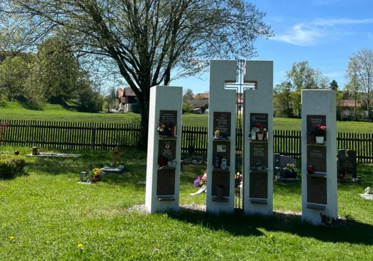 Urnenstelen mit Kreuz vor einem blühenden Baum auf dem Friedhof Degerndorf