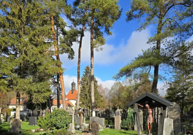 Grabfeld mit Kruzifix unter hohen Kiefern auf dem Waldfriedhof Bad Tölz
