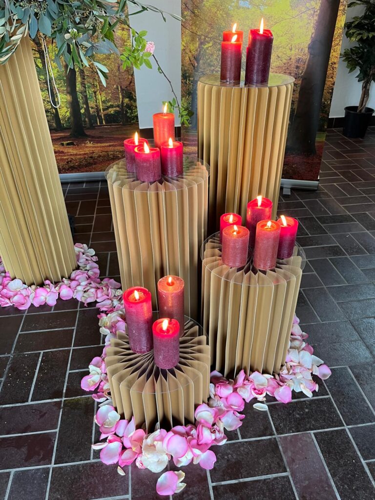 Trauerdekoration mit gefalteten Papiersäulen, roten Kerzen und Rosenblättern