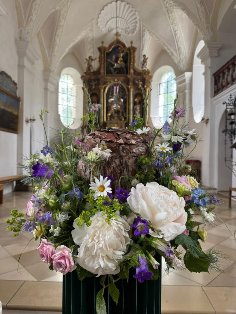 Urne inmitten von Blumenschmuck mit weißen Pfingstrosen und blauen Blüten in der Kirche Holzhausen