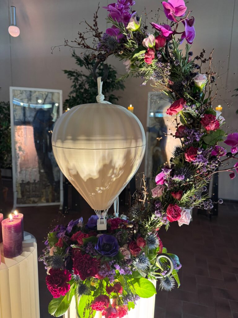 Urne in Form eines Heißluftballons mit Blumenbogen aus roten und rosa Blüten