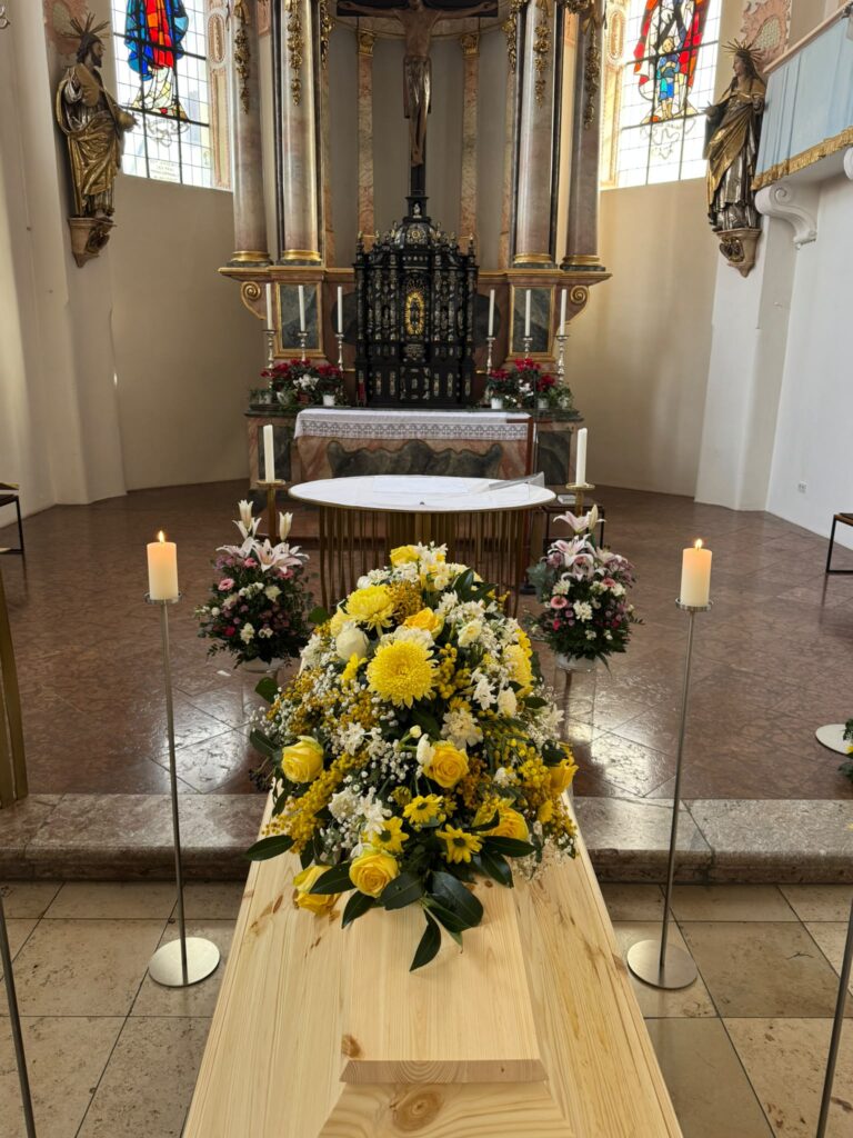 Sargbukett mit gelben Blumen auf einem Holzsarg vor dem Altar einer Kirche