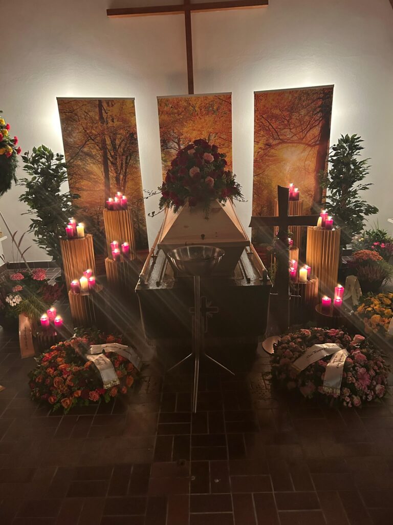 Aufgebahrter Sarg mit Blumenschmuck, Kränzen und Kerzen in der Aussegnungshalle