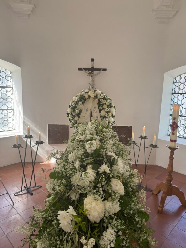 Sarg mit weißem Blumenschmuck in einer Kapelle mit Kruzifix