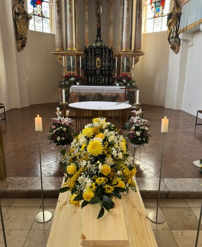 Sargbukett mit gelben Blumen auf einem Holzsarg vor dem Altar einer Kirche