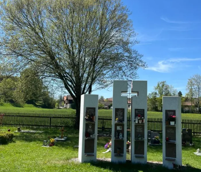 Urnenstelen mit Kreuz vor einem blühenden Baum auf dem Friedhof Degerndorf